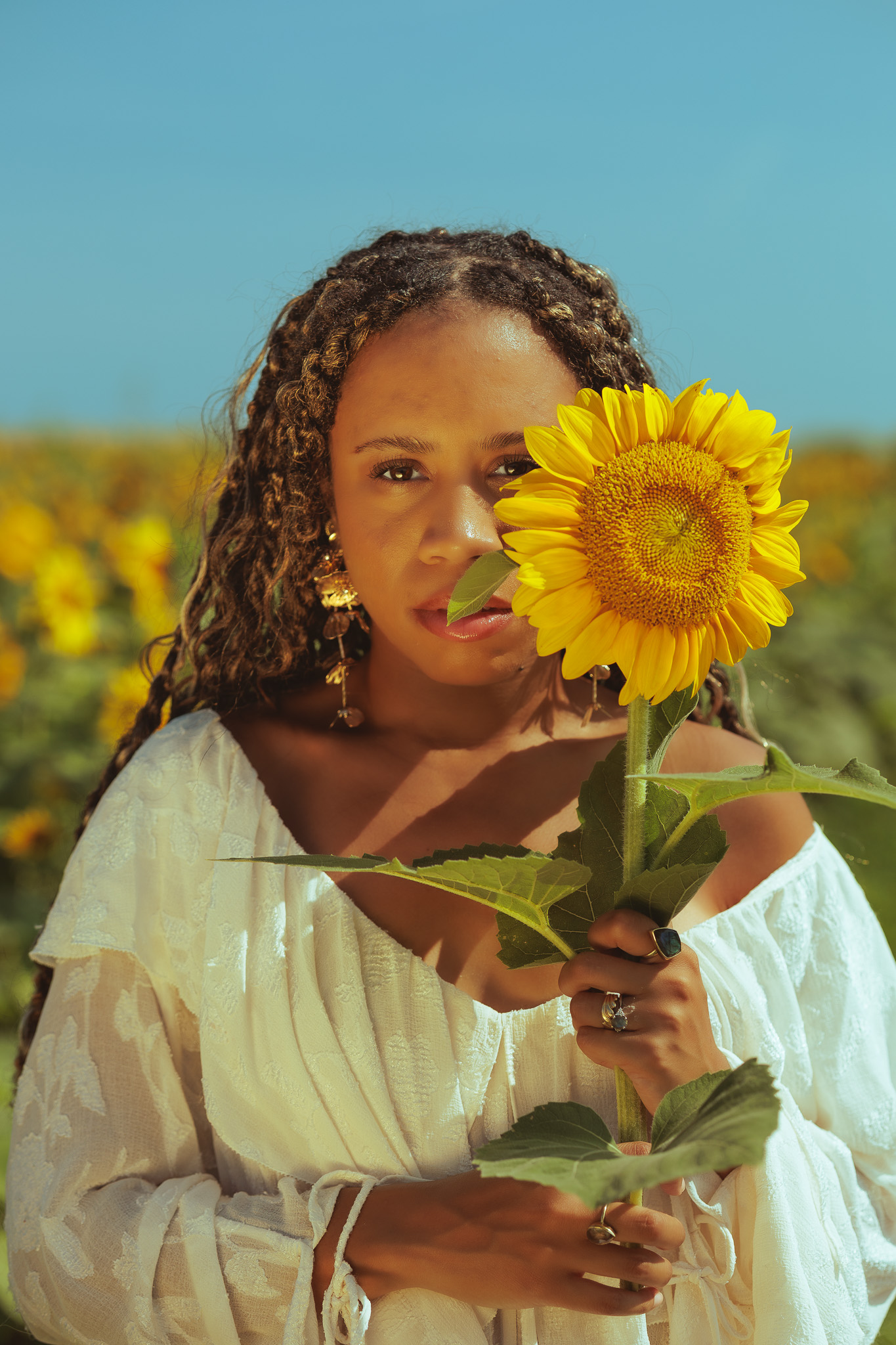 Two women embracing warmly in the sunflower field, both in white dresses